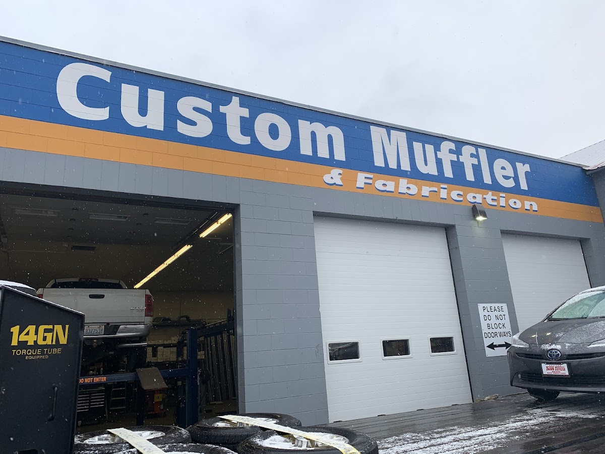 Custom Muffler & Fabrication sign over an open shop bay with a truck on the lift